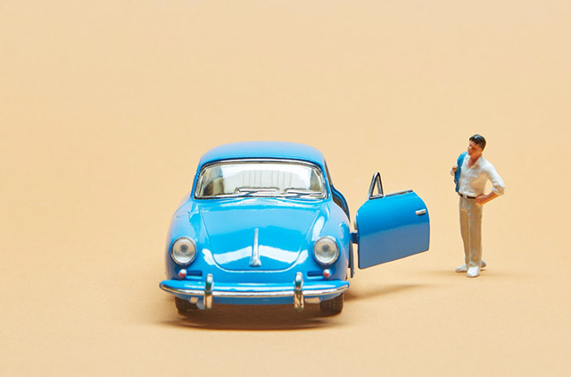 Small, blue VW with man standing next to open door.
